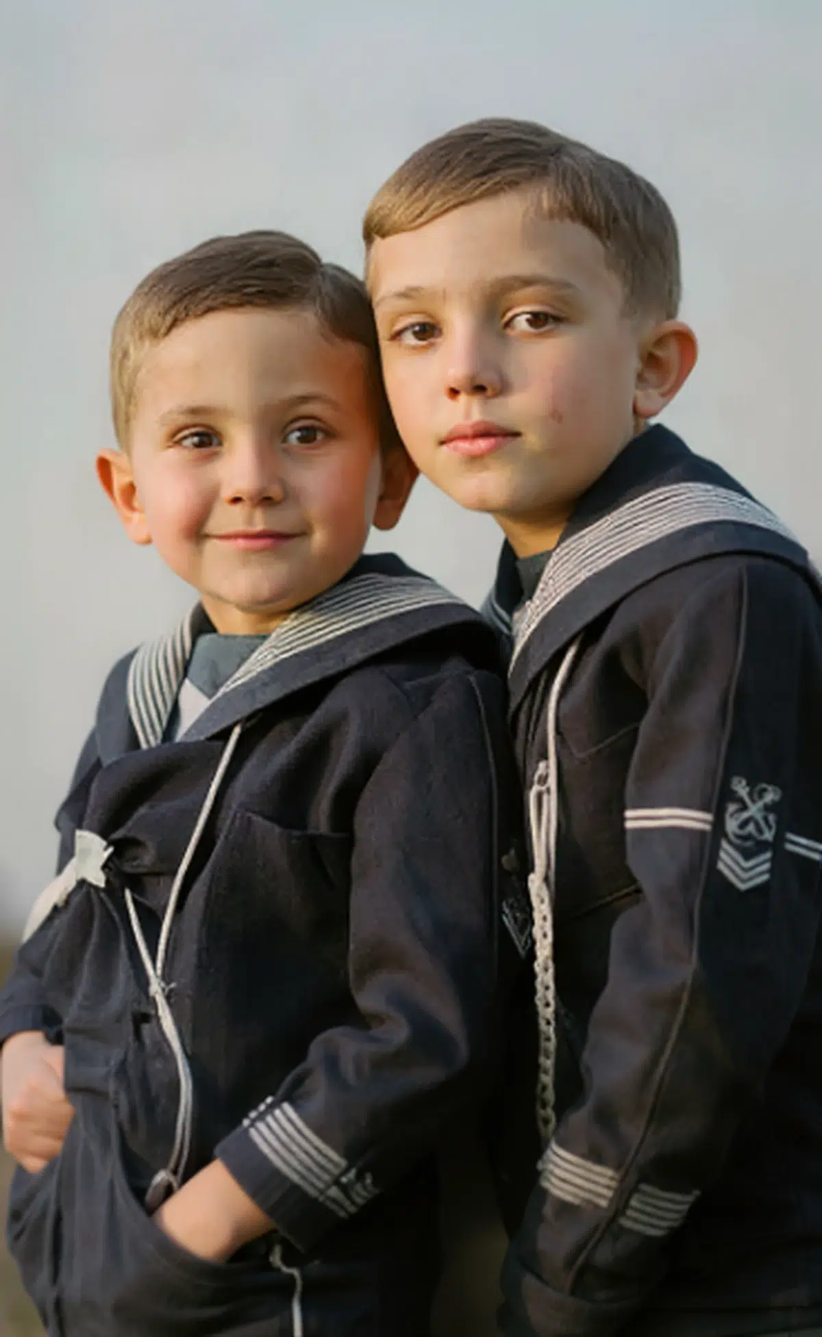 a clear, restored color portrait of two young boys in dark sailor outfits, with natural skin tones and a soft, out-of-focus background
