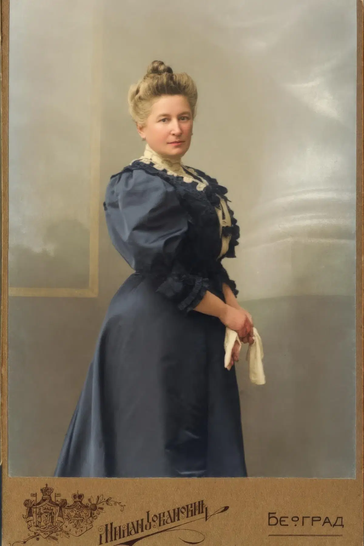 a restored, full-color studio portrait of a victorian-era woman with her hair in an updo, wearing a dark blue dress with lace details, and holding white gloves